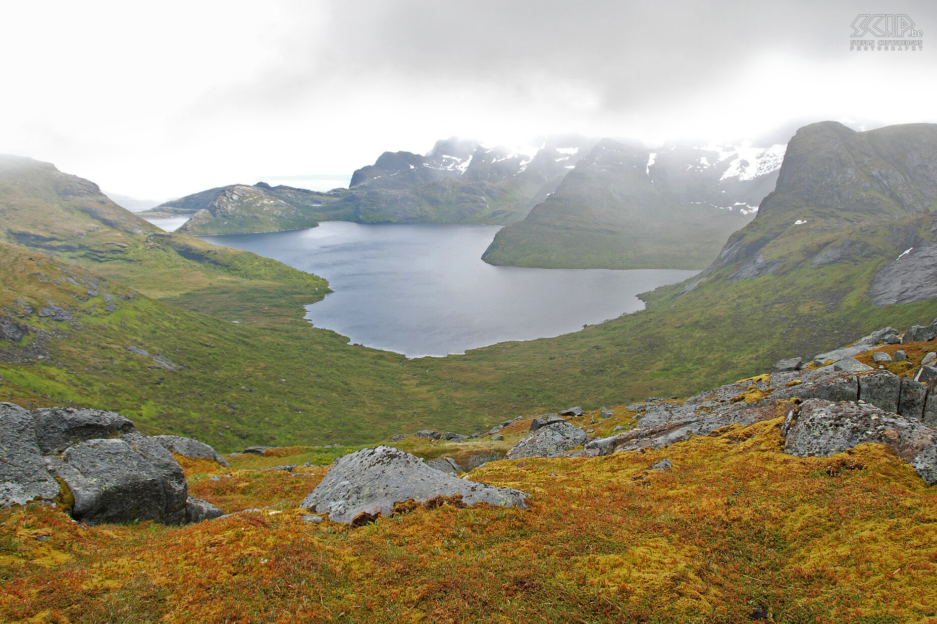 Van Kjerkfjorden naar Selfjorden Vanuit Hamnøy namen we een boot naar het dorpje Kjerkfjorden, van waaraf onze driedaagse trekking begon. Ook deze dag is regenachtig, maar toch geeft de mist, de regen en de zon die af en toe doorheen de wolken komt een speciale sfeer. Hier staan we op de top boven het Solbjørnvatnet meer. De verdere tocht doorheen de venen naar Selfjorden was vooral glad en drassig. Stefan Cruysberghs